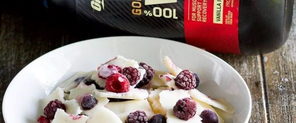 Optimum Nutrition Gold Standard 100% Whey protein powder in vanilla ice cream flavor, next to a bowl of berries and yogurt
