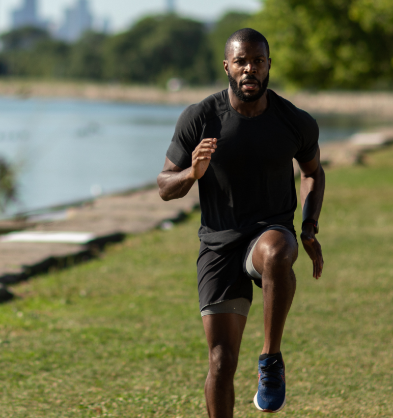 Man running outdoors near a body of water, wearing athletic clothing