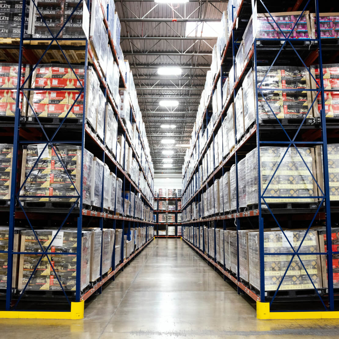 Warehouse shelves filled with boxes of Optimum Nutrition products, including Gold Standard 100% Whey Protein and Serious Mass Weight Gainer